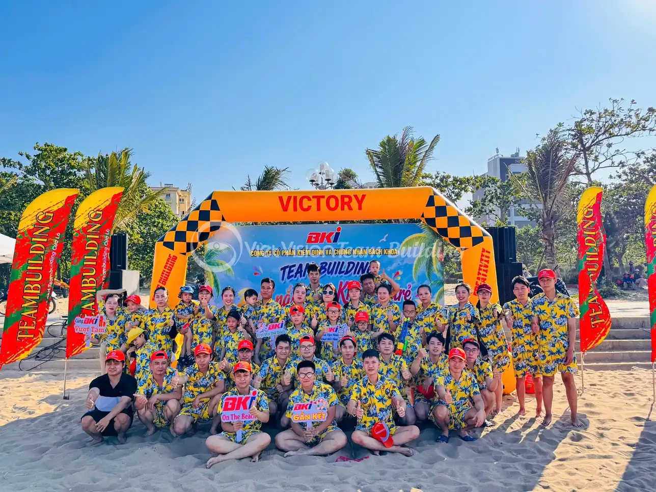 Tập thể công ty chụp ảnh trước cổng hơi và banner team building trên bãi biển