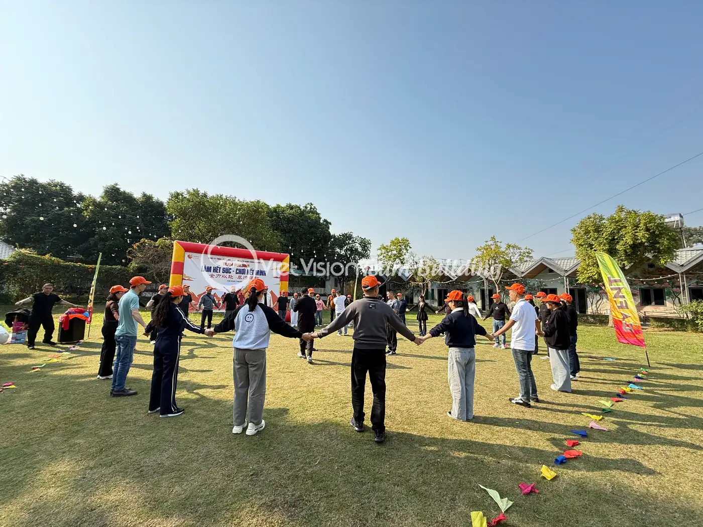 Nhiều đội chơi đứng trên sân cỏ rộng trước backdrop team building