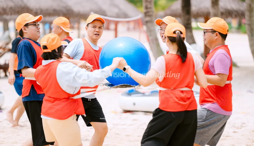 Đội nhân viên phối hợp giữ bóng trong trò chơi team building gắn kết nhân viên trên bãi biển