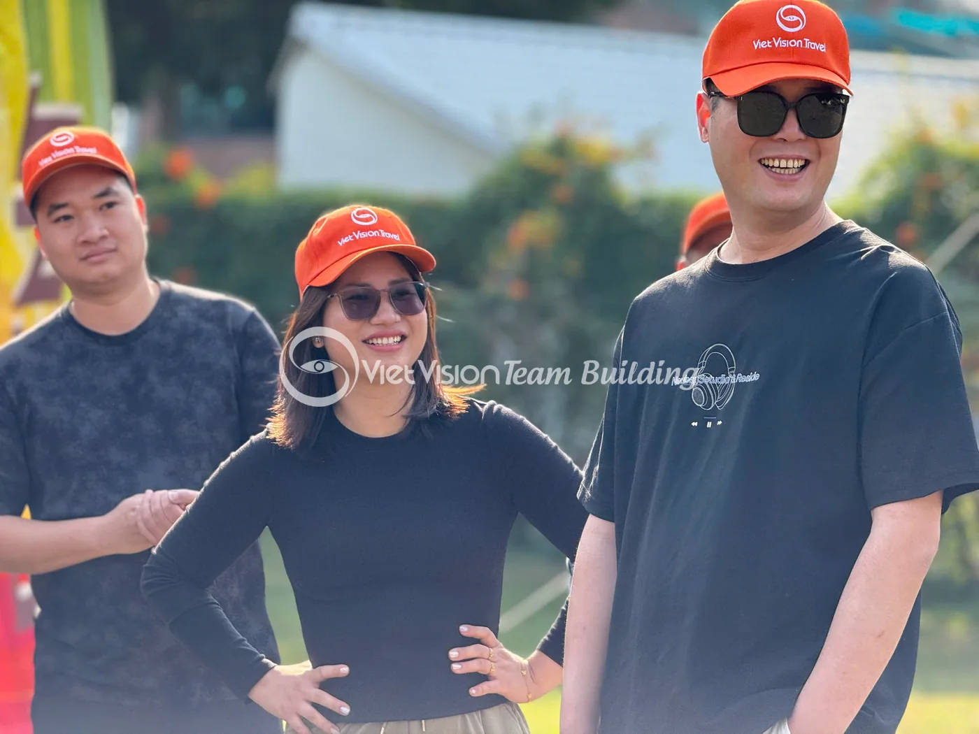 Nhóm thành viên mặc áo đen và mũ cam đứng cùng nhau tại sân team building